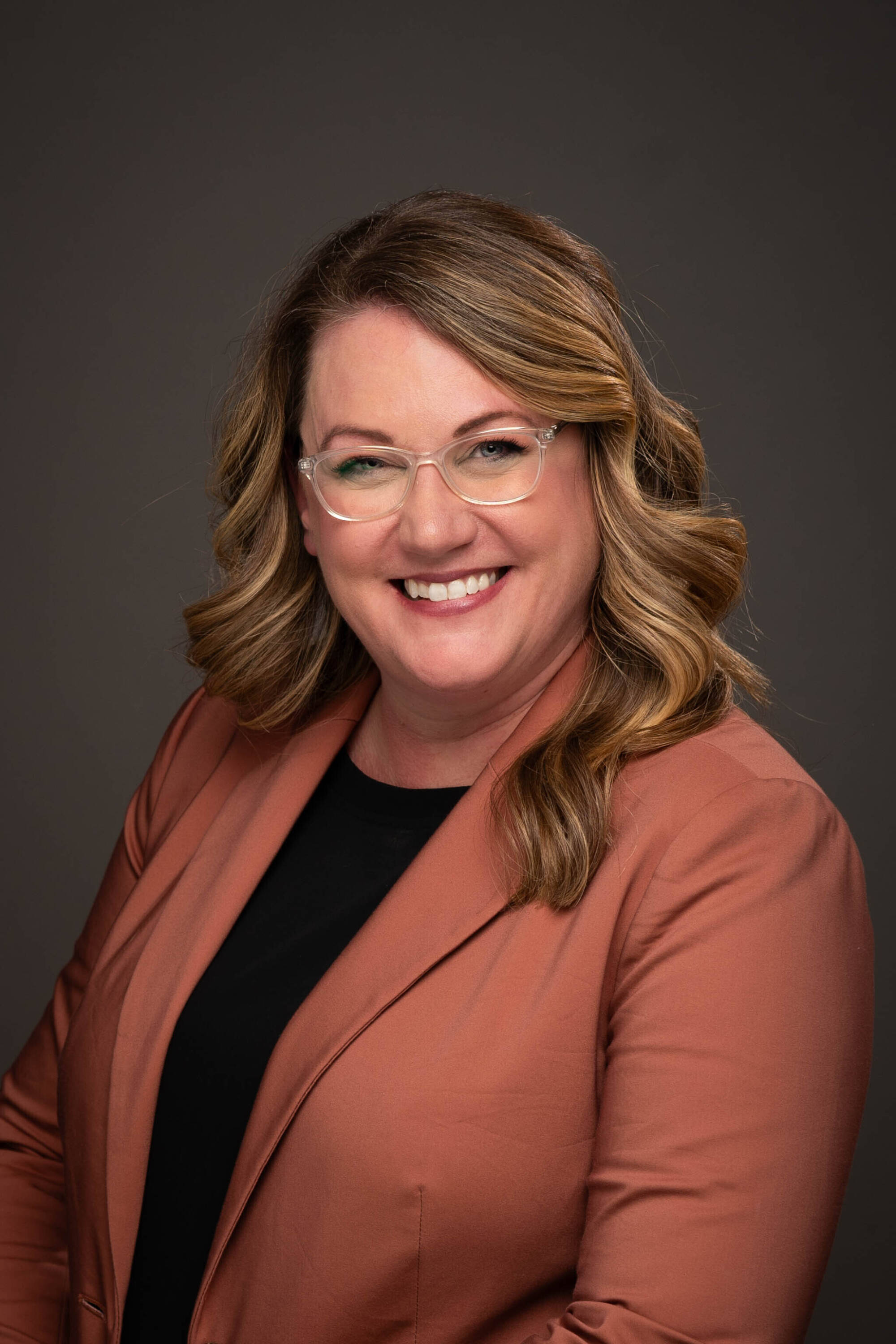 Liz Lienau in burnt orange blazer and black shirt, with glasses